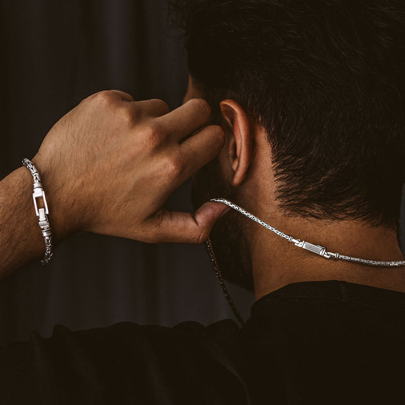 Een man die zich omdraait, met in zijn hand de Turath Byzantine-ketting van sterlingzilver, terwijl hij een Ninetwofive heren armband draagt.