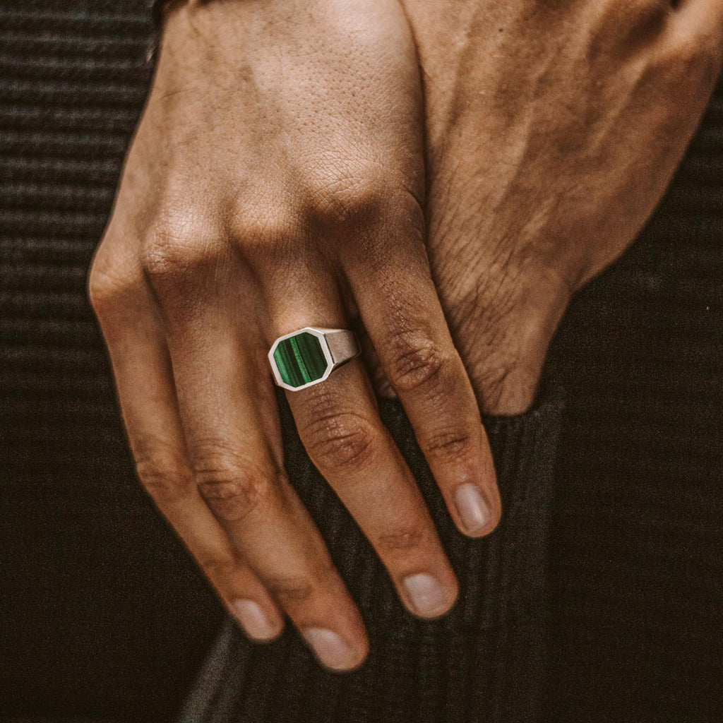 Een man draagt een ring met een groene steen.