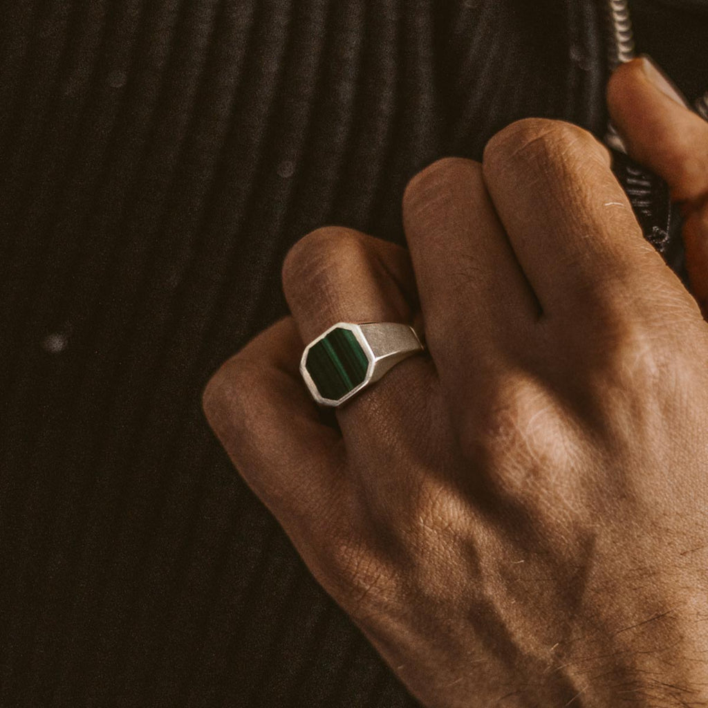 Een man draagt een ring met een groene steen.
