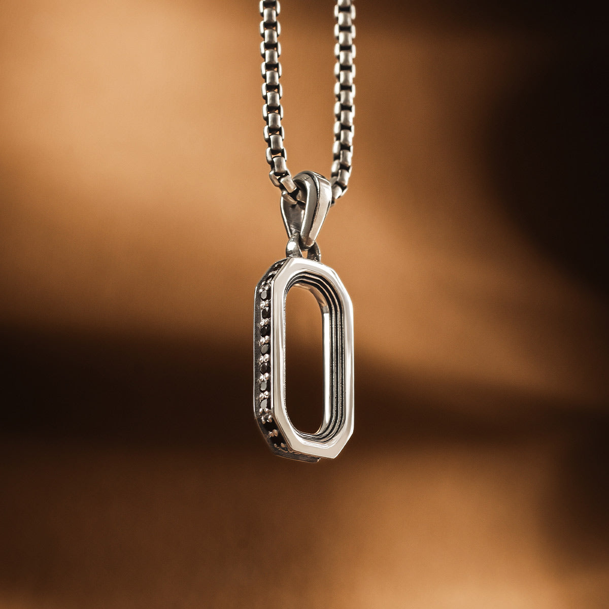 Vue de face du pendentif en argent de l'arc de Durwās sur fond brun. Ninetwofive