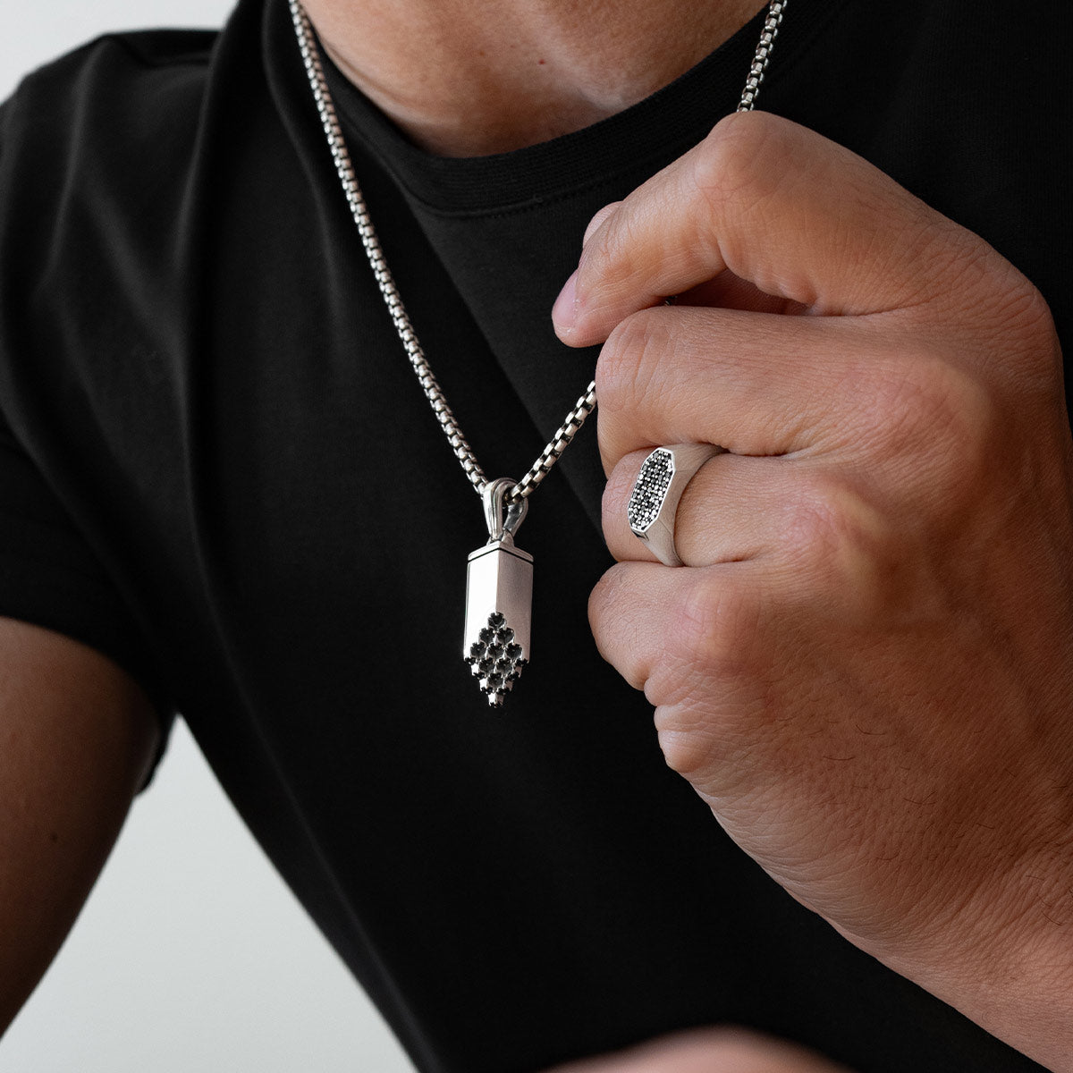 Ein Model hält einen silbernen Muqarnas-Anhänger in der Hand und trägt den Herren-Siegelring „Azhar“ von Ninetwofive Nahaufnahme Ninetwofive .