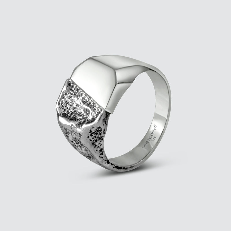 Foto van een zilveren heren ring onder een hoek, waarop de asymmetrische vorm te zien is