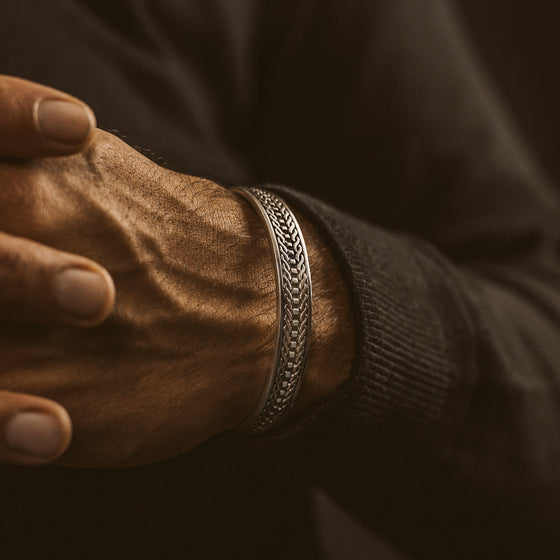 Een man die een geoxideerde sterlingzilveren armband van Fariq draagt, met een gegraveerd patroon.