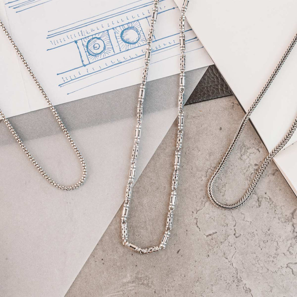 Trois colliers en chaîne argentée reposant sur une feuille de papier.