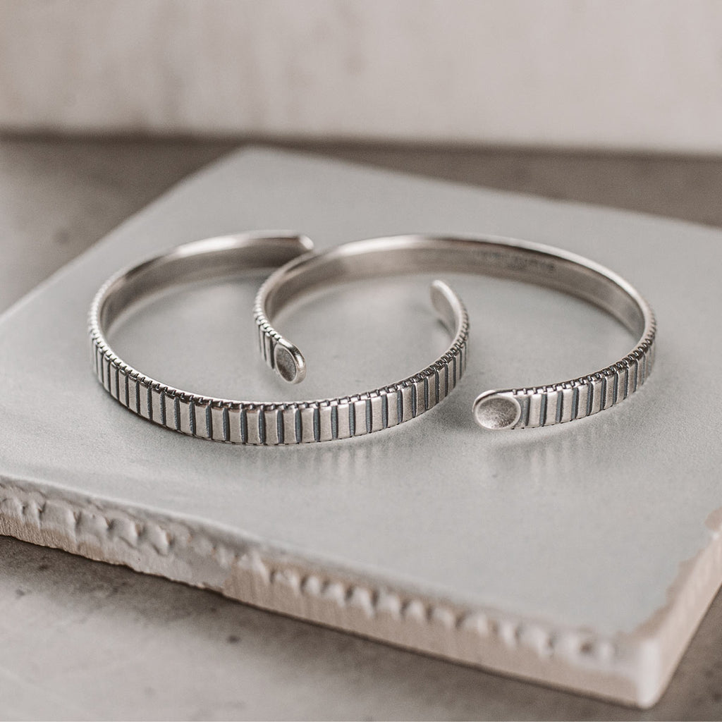A pair of silver cuff bracelets on a tile.