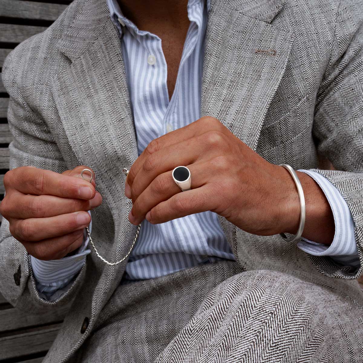 Model wearing Adil sterling silver black onyx men’s signet ring and holding mens bracelet from Ninetwofive.