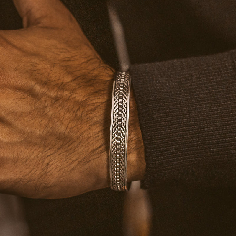 Een man draagt de Fariq geoxideerde 925 sterling zilveren cuff armband met een gegraveerd patroon.