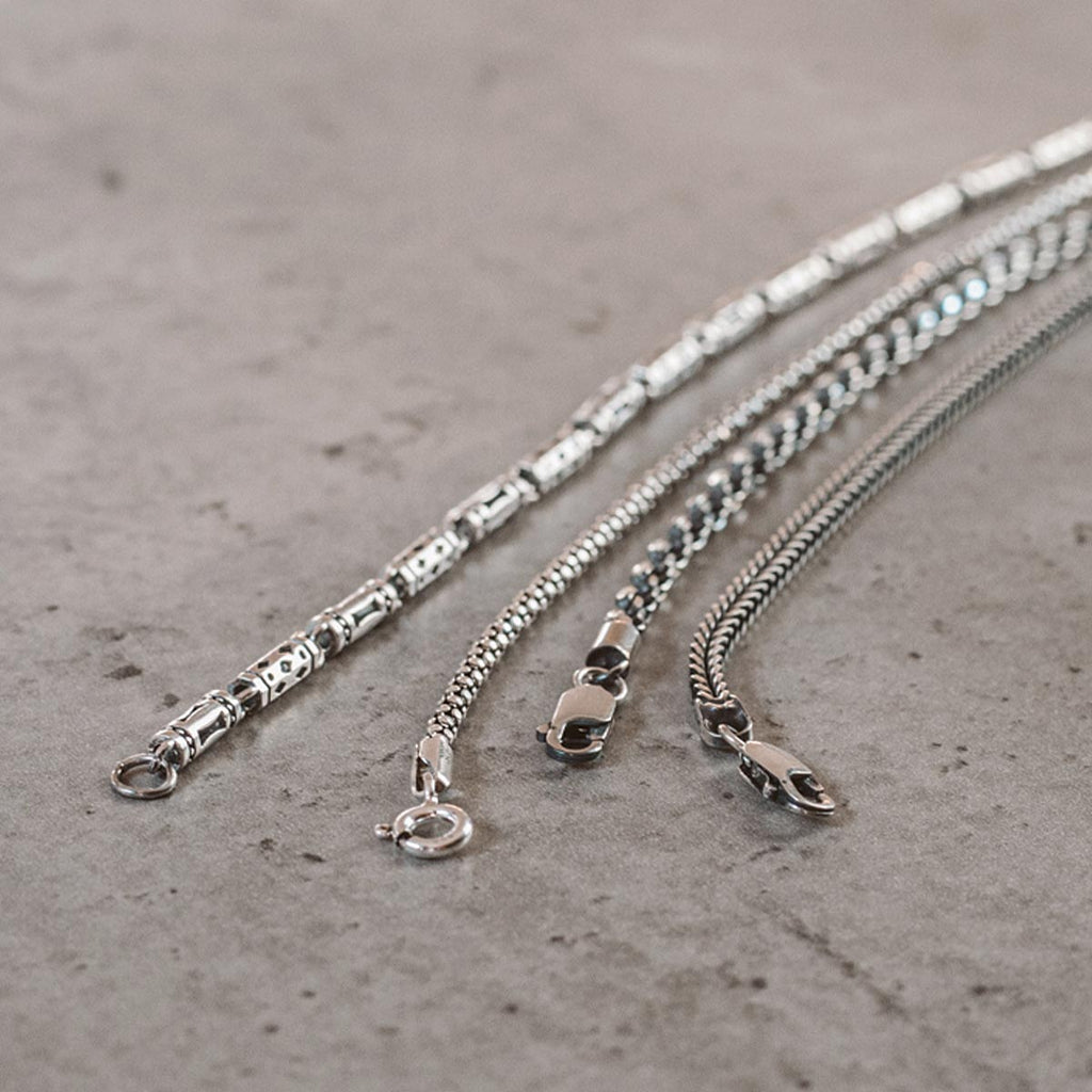 Three silver chain necklaces on a surface.