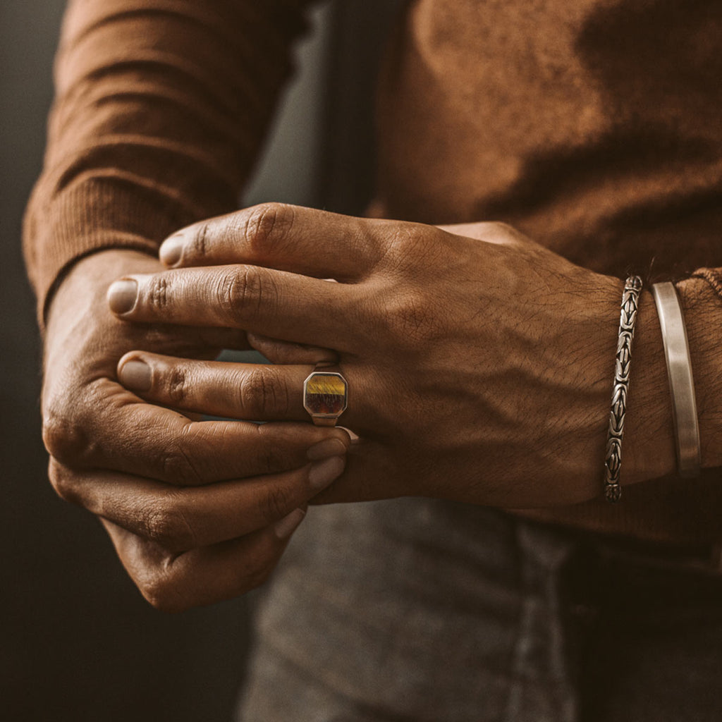 A man wearing a gold ring and a brown sweater.