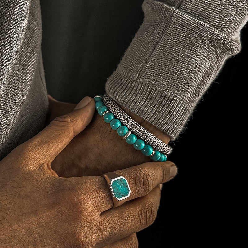 Man in grijze trui draagt aan de ene hand een zegelring, en aan de andere de Nuri kralenarmband met turkoois en een zilveren band.
