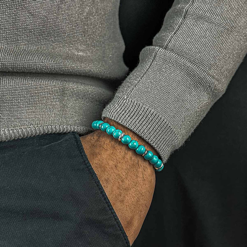 Man in grijze trui draagt de Nuri heren kralenarmband, met zijn hand in een zwarte broekzak.