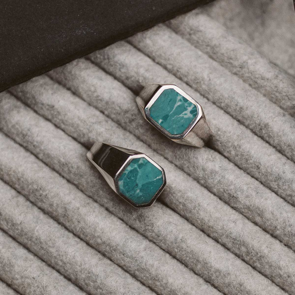 A pair of turquoise stone ring sitting on top of a grey cloth.