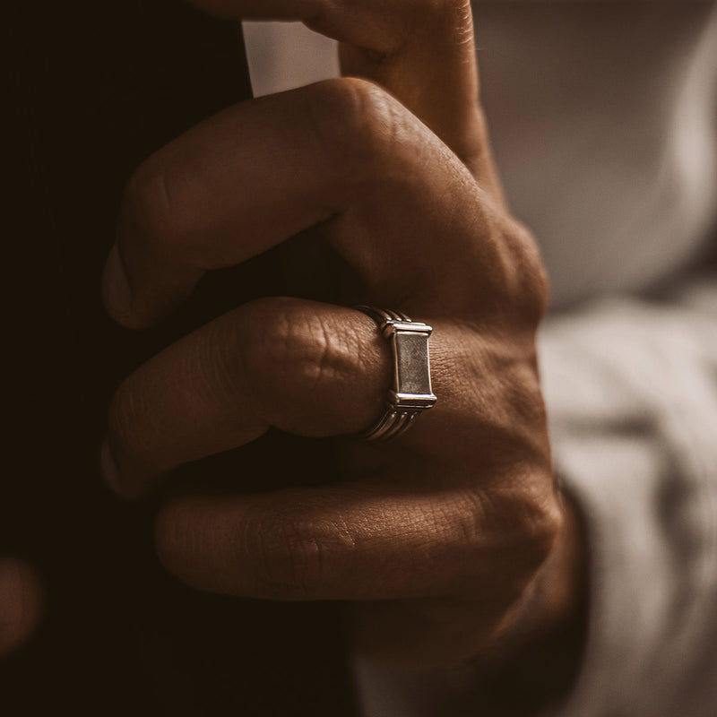 Die Hand eines Mannes, die behutsam einen gravierten Imad-Herrenring aus Sterlingsilber von Ninetwofive umschließt.