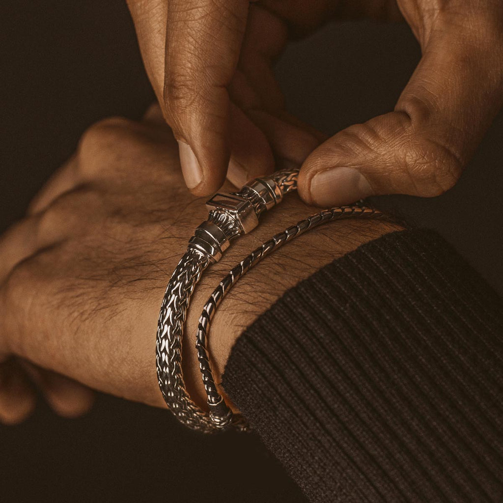 A man is putting on a NineTwoFive - Mirza Sterling Silver Braided Bracelet 7mm on his wrist.