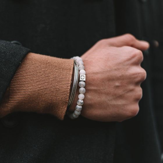 Man die de witte Abyad-armband voor heren draagt, met witte, verweerde stenen kralen en een zilveren manchet, van Ninetwofive.