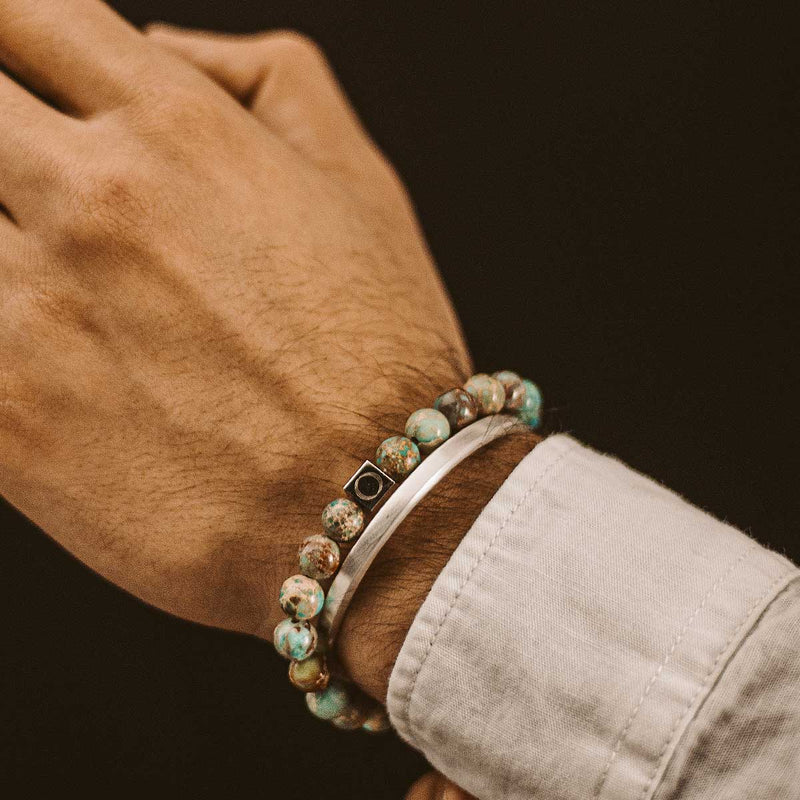 Model in een wit overhemd, met de Ninetwofive Alfriuz turquoise kralenarmband voor heren, gecombineerd met een zilveren manchet.