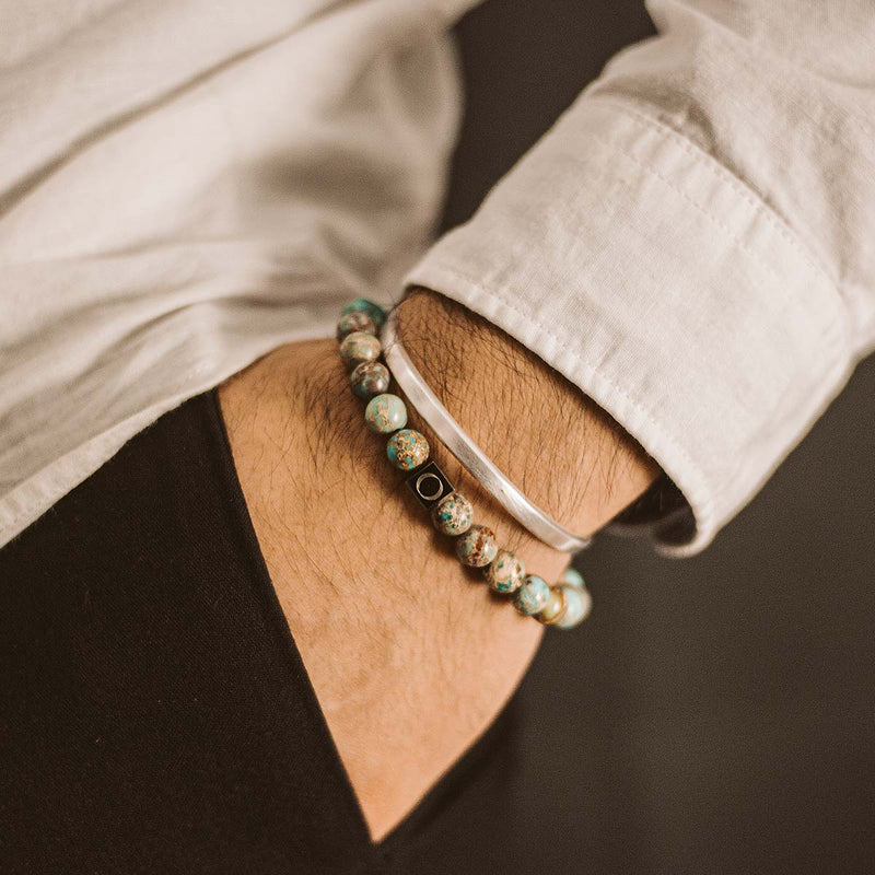 Een man in een wit overhemd draagt de turkooizen Ninetwofive Alfiruz kralenarmband voor heren en een Cuff, met zijn hand in zijn zwarte broekzak.