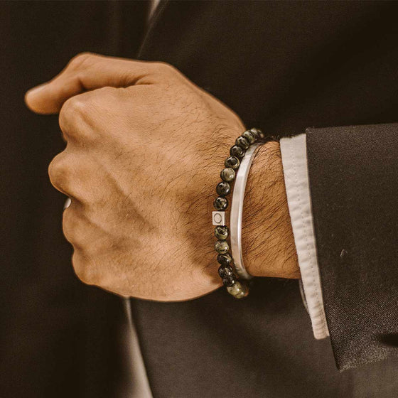 Man in a black and white suit displaying the Ahgdar mens green beaded bracelet layered with a silver cuff by Ninetwofive.