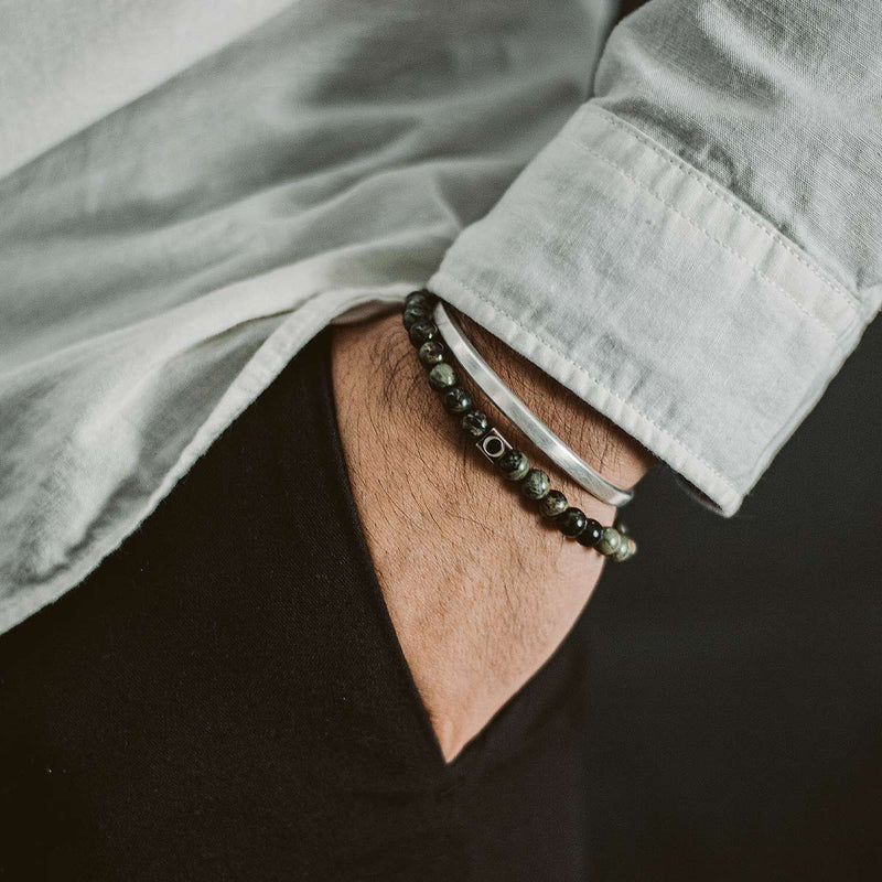 Model in white shirt wearing the Ninetwofive Ahgdar mens green beaded bracelet and a silver cuff, with his hand in his black trouser pocket.