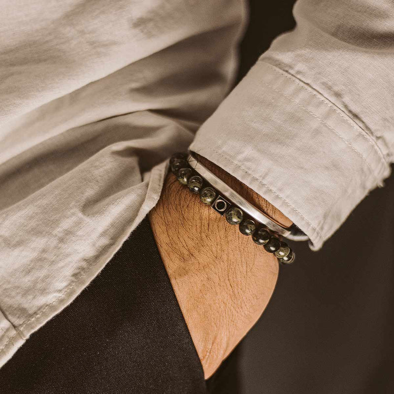 A man in white shirt wearing the Ninetwofive Ahgdar mens green beaded bracelet and a silver cuff, with his hand in his black trouser pocket.