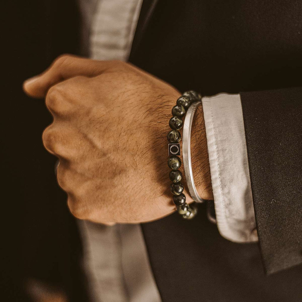 Een man draagt een zwart pak en een Ahgdar - Groene Kralen Armband 8mm die zijn uiterlijk meer gewicht geeft.