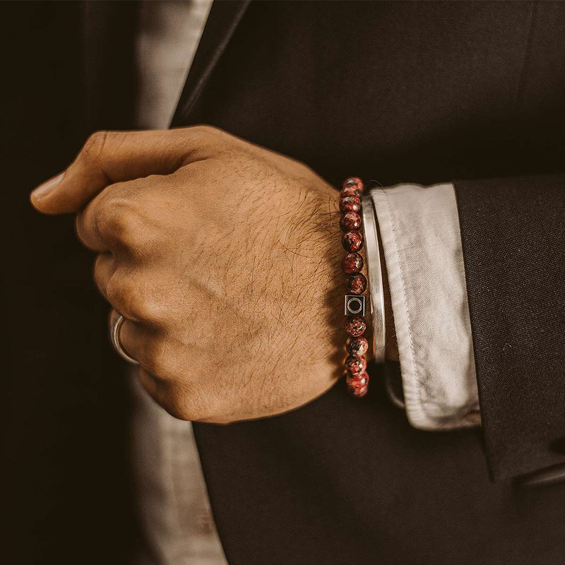 Model in a black suit displaying the Ninetwofive Ahmar red beaded men's bracelet layered with a silver cuff. 