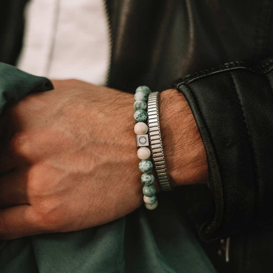 Akhdir men's jade beaded bracelet and silver bangle worn by a man in a black jacket holding green cloth, Ninetwofive.