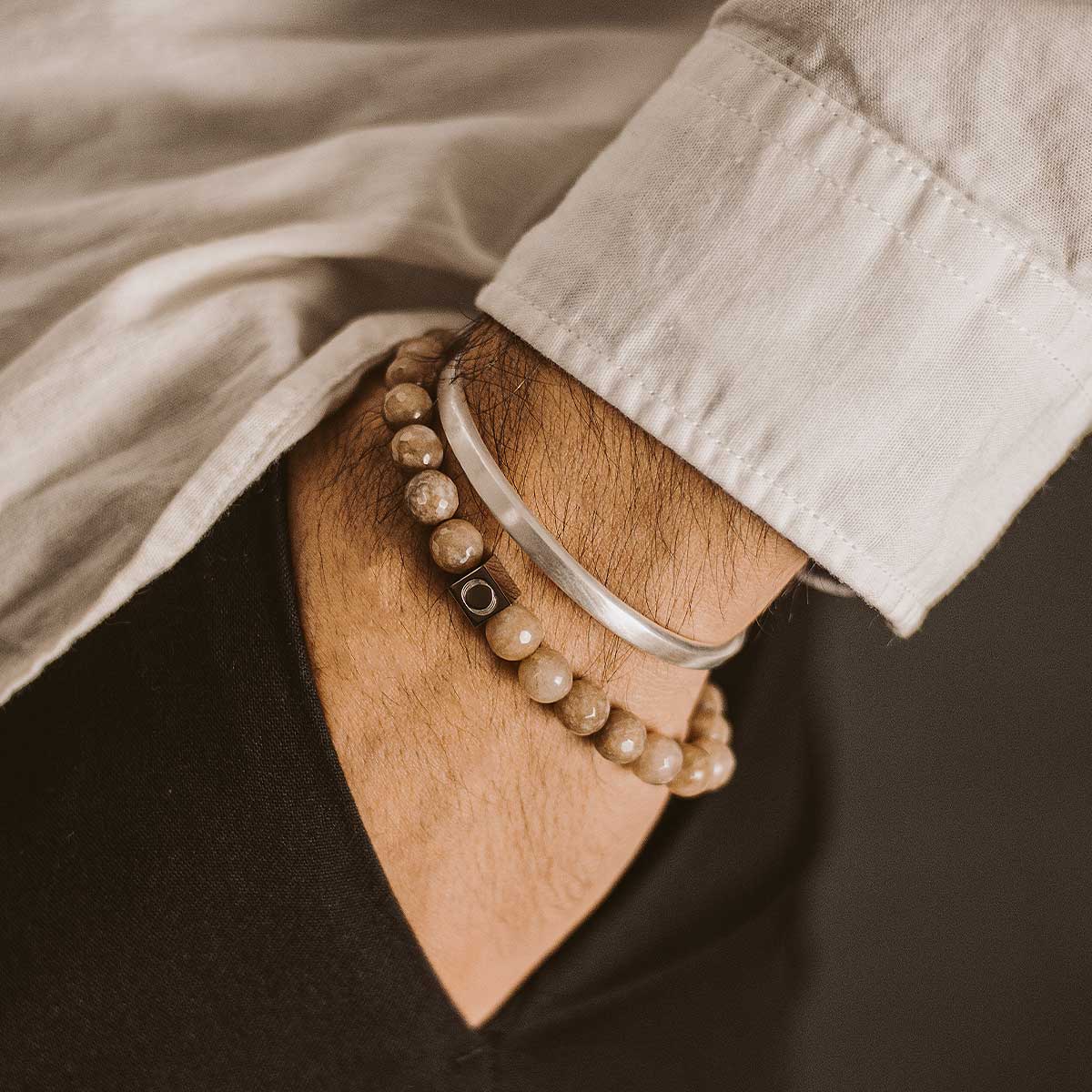 Das Handgelenk eines Mannes, geschmückt mit zwei Albij - Beige Beaded Bracelets 8mm, die die exquisite Schönheit und die einzigartige Dicke der Accessoires zur Geltung bringen.