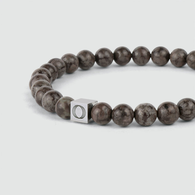 Close-up vanuit een zijdelingse hoek van de bruine Albuna-armband met kralen voor heren, waarop de sneeuwvloksteen en het ‘Ninetwofive’-logo te zien zijn.