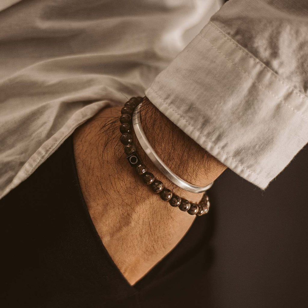 Das Handgelenk eines Mannes mit einem Albuna - Brown Beaded Bracelet 6mm daran.