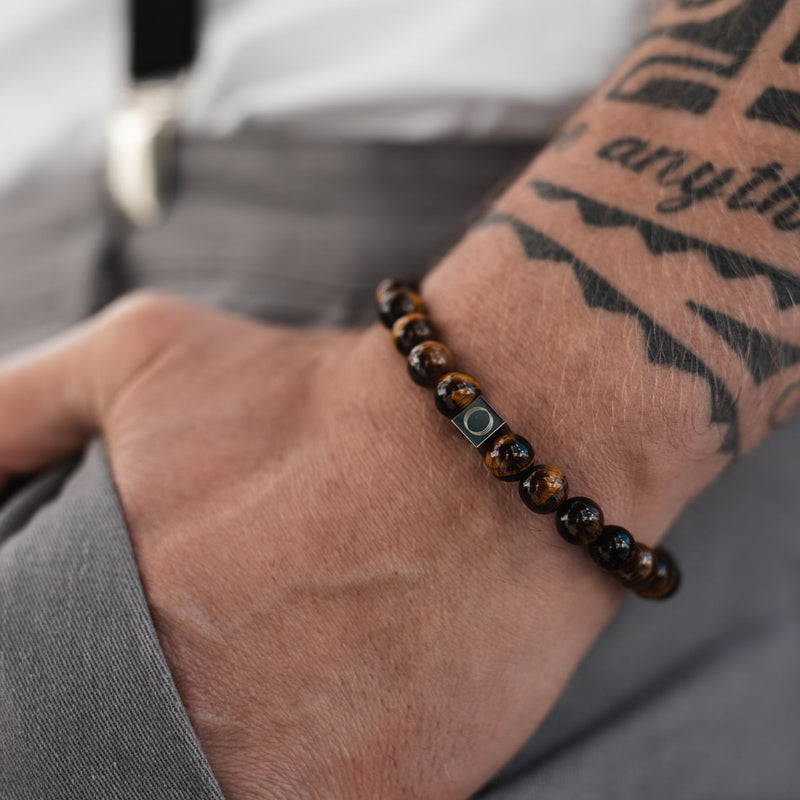 Man showcasing the Ninetwofive Alnamr tiger eye beaded bracelet. He stands casually with his hand in his gray pocket.