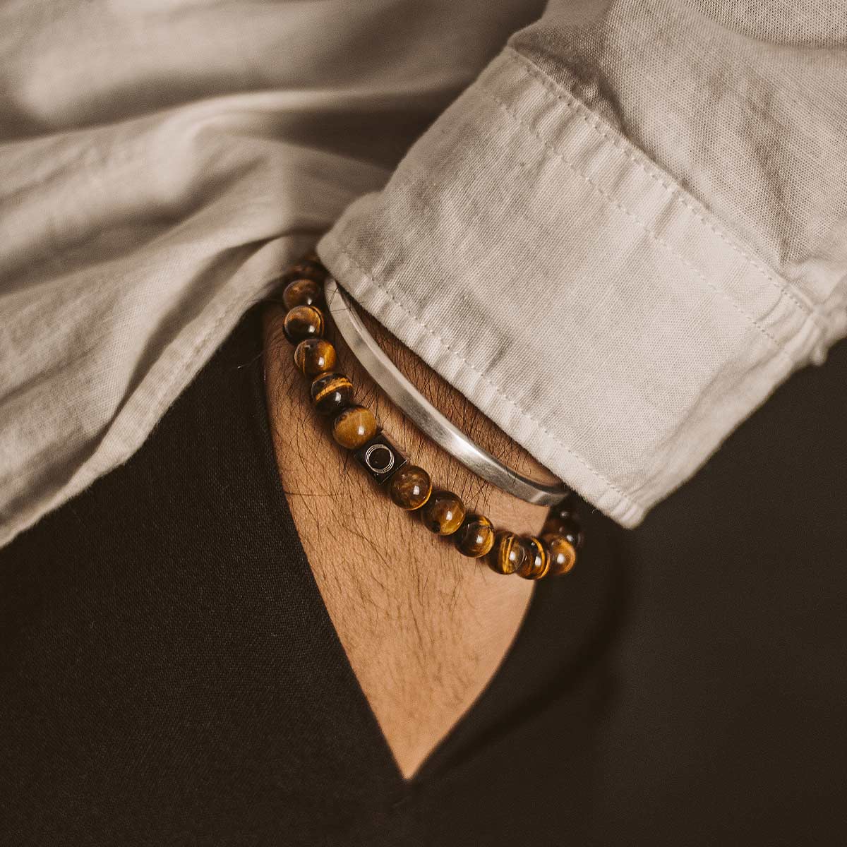 Een man draagt de Alnamr - Tijgeroog Kralen Armband 8mm, met tijgeroogsteen.