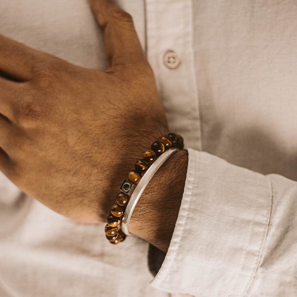 Een man draagt de Alnamr - Tijgeroog Kralen Armband 8mm. De armband is gemaakt met tijgeroogsteen en heeft een dikte van 8 mm.