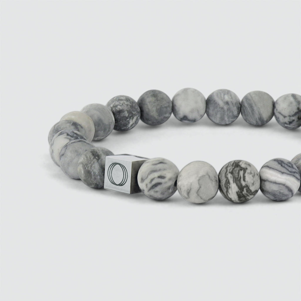 Een grijze kralenarmband met een zilveren sluiting die 10 gram weegt.