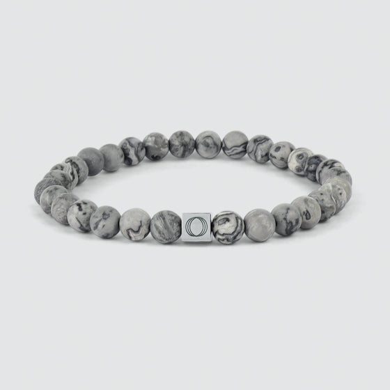 Ein graues Perlenarmband von Alrazas mit einer Marmorperle und eingraviertem „Ninetwofive“-Logo.