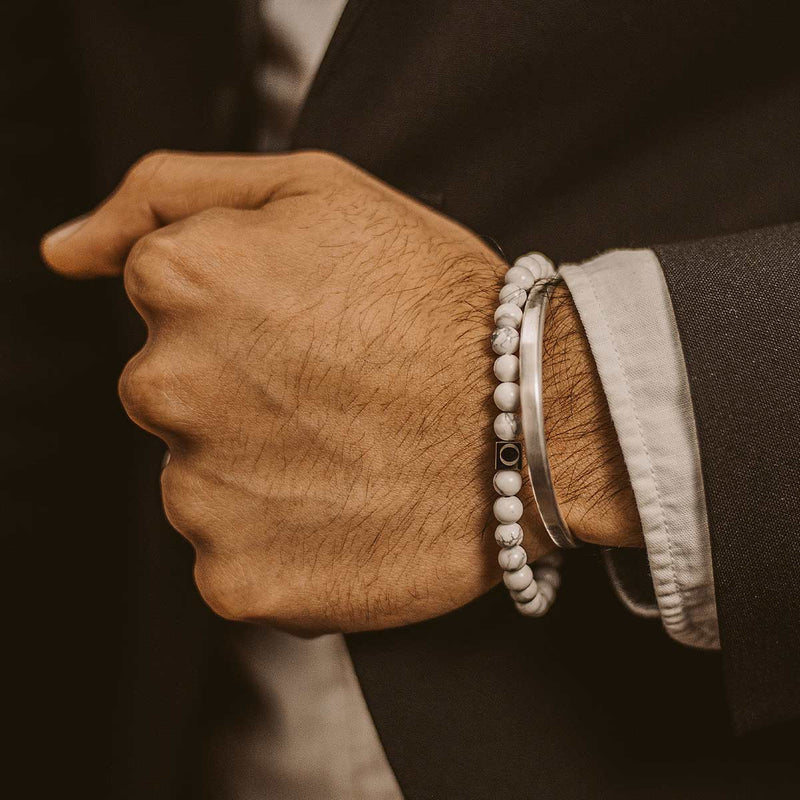 A man in a black suit is wearing Alrukham mens white beaded bracelet and a sterling silver cuff by Ninetwofive.