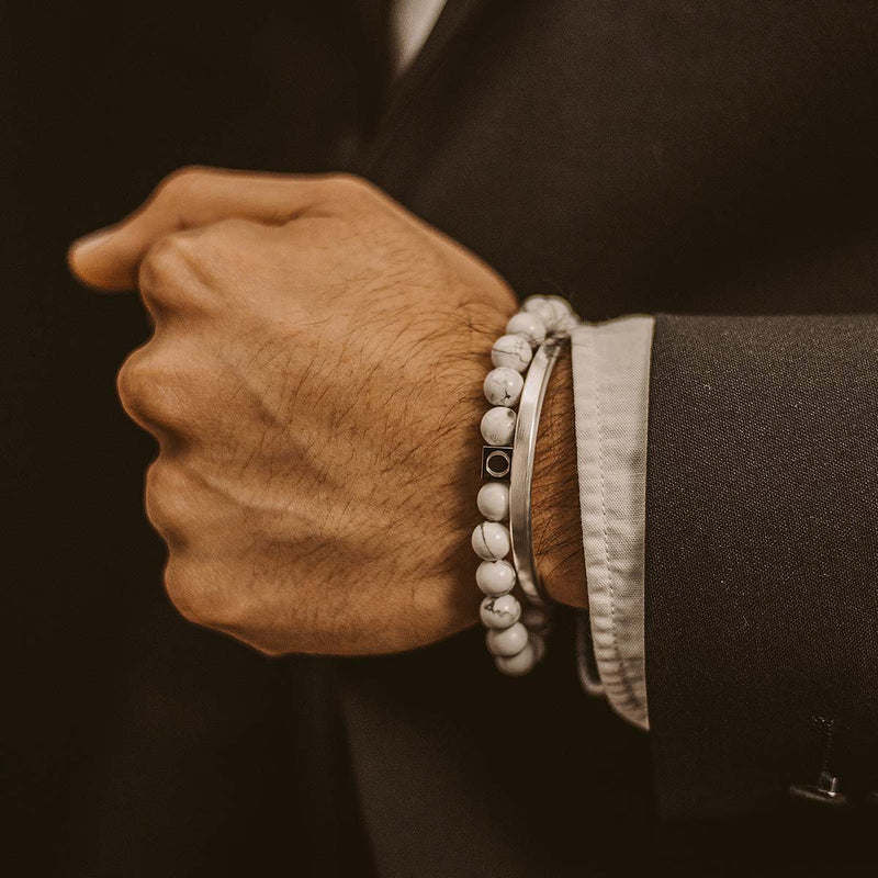 Het model in een zwart-wit pak draagt een witte kralenarmband van Alrukham voor heren en een manchet van sterlingzilver van Ninetwofive.