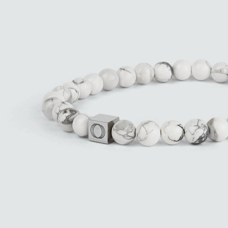 Close up side angle of the Alrukham mens white beaded bracelet in a contrasting background, highlighting the beads and the Ninetwofive logo.