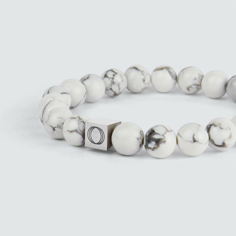 Close-up vanuit een zijdelingse hoek van de Alrukham-armband voor heren met kralen tegen een contrasterende achtergrond, waarbij het witte marmer en het logo ‘Ninetwofive’ goed tot hun recht komen.