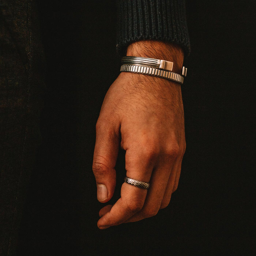 A man's hand adorned with a silver ring and an Arkan - Sterling Silver Bangle Bracelet 8mm.