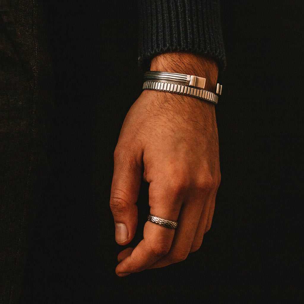 A man sporting a sleek pair of silver cuffs, reminiscent of the Kenan - Sterling Silver Bangle Bracelet 7mm.