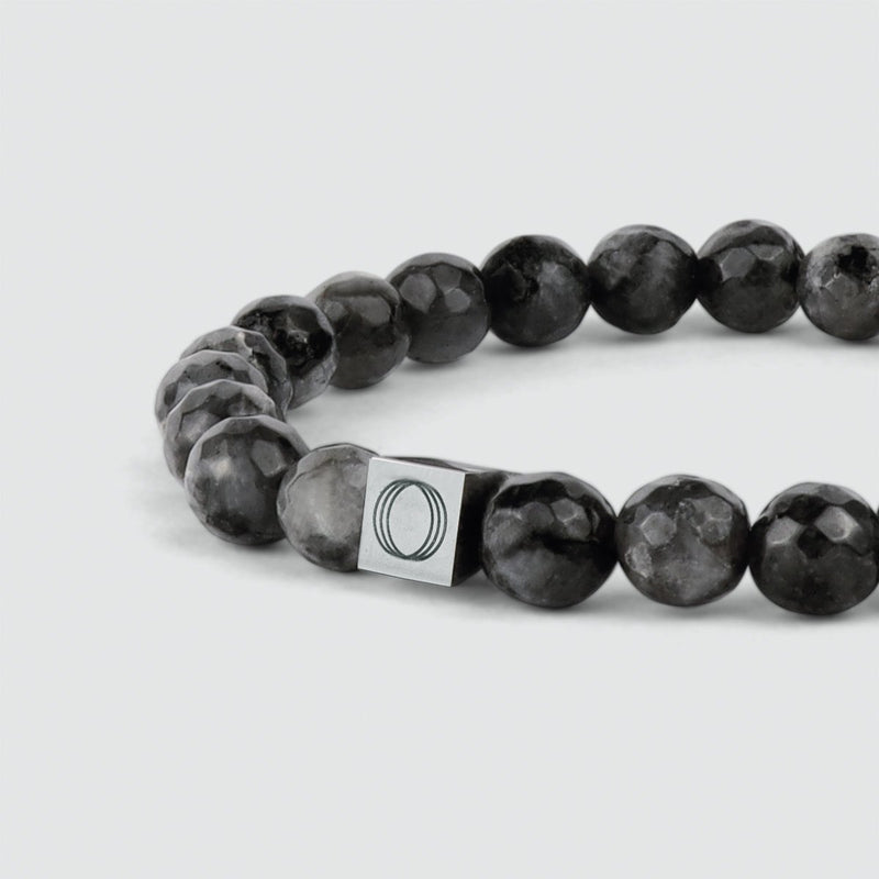 Close up angle view of the Aswad mens black beaded bracelet and showing the engraved Ninetwofive logo.