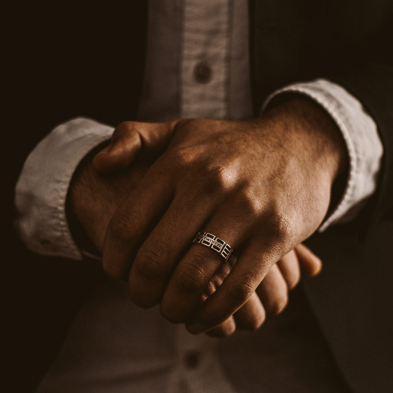 Ein Mann im Anzug trägt einen gravierten Ninetwofive Ayman oxidierten Sterling Silber Herrenring am Ringfinger.