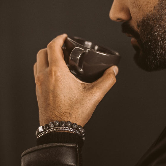 Bearded man wearing the Aswad black beaded bracelet and a silver bracelet from Ninetwofive, while holding a black mug.