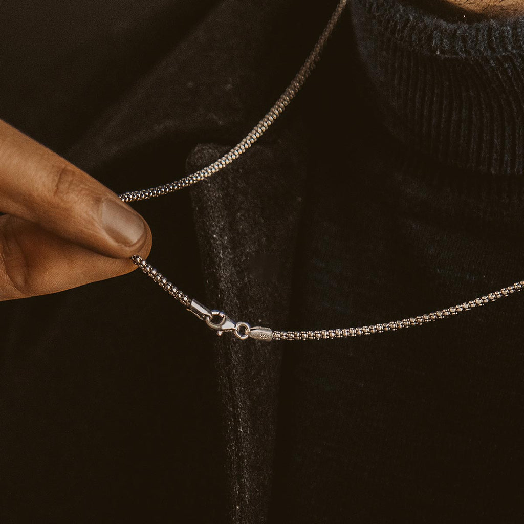 A man is putting on a Naseeb - Elegant Sterling Silver Chain Necklace 2.5mm of adjustable length.