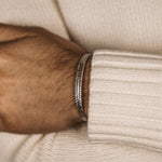 Un homme portant un pull blanc et un Zahir - Thin Sterling Silver Feather Jonc 6mm.