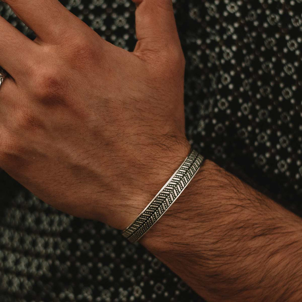 A man wearing a Danyal - Oxidized Sterling Silver Bangle Bracelet 9mm with an intricate pattern engraved on it.