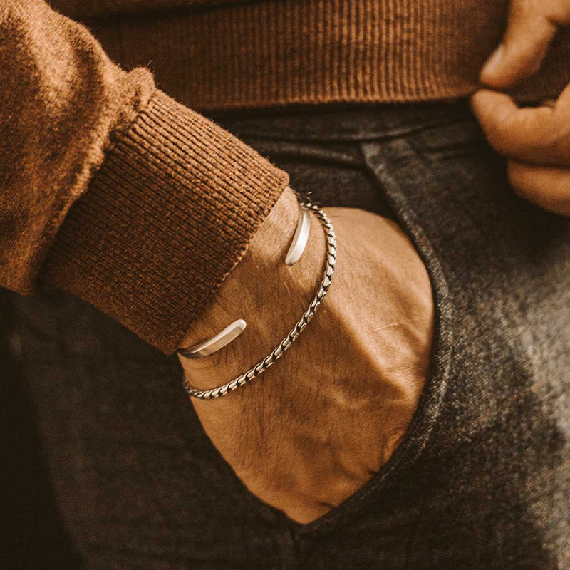 Een man die een paar Ninetwofive-armbanden draagt, waaronder een gepersonaliseerde en gegraveerde minimalistische heren armband van sterlingzilver van Emir.
