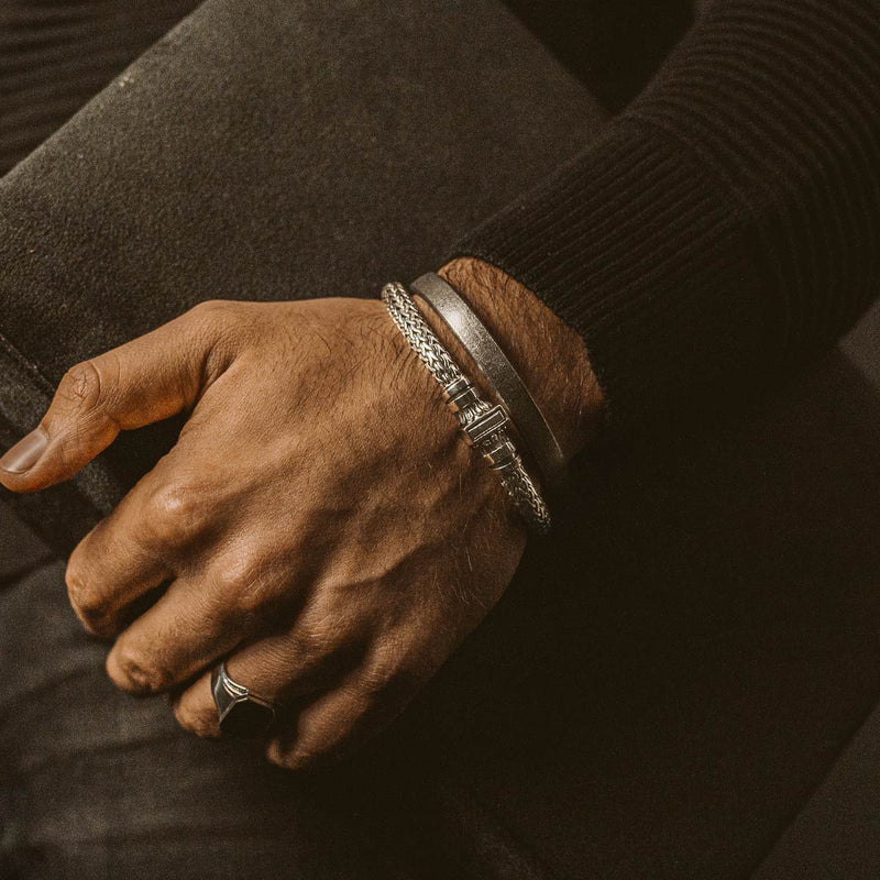 A man's hand holding a book and a personalized Mirza sterling silver mens bracelet