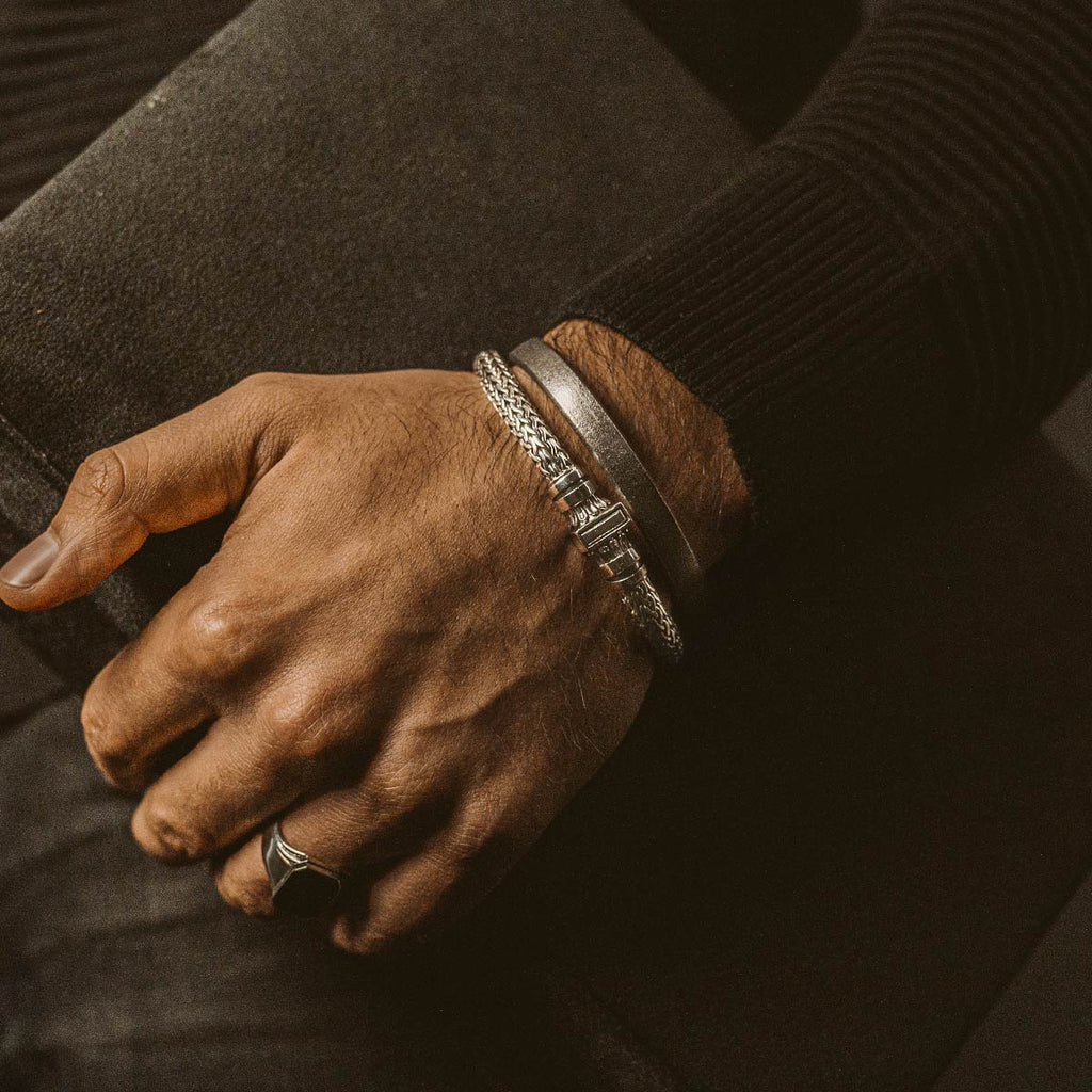 Die Hand eines Mannes hält ein Buch und ein personalisiertes NineTwoFive Mirza - Sterling Silver Braided Bracelet 7mm.